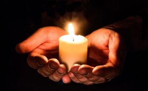 The photo shows a person holding a white candle in his hands.