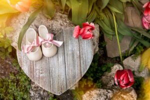 The photo shows a heart carved from wood. There are flowers in the background.